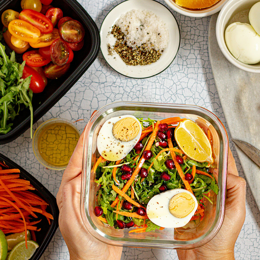 female hands holding healthy meal prep container in bright and cheerful kitchen