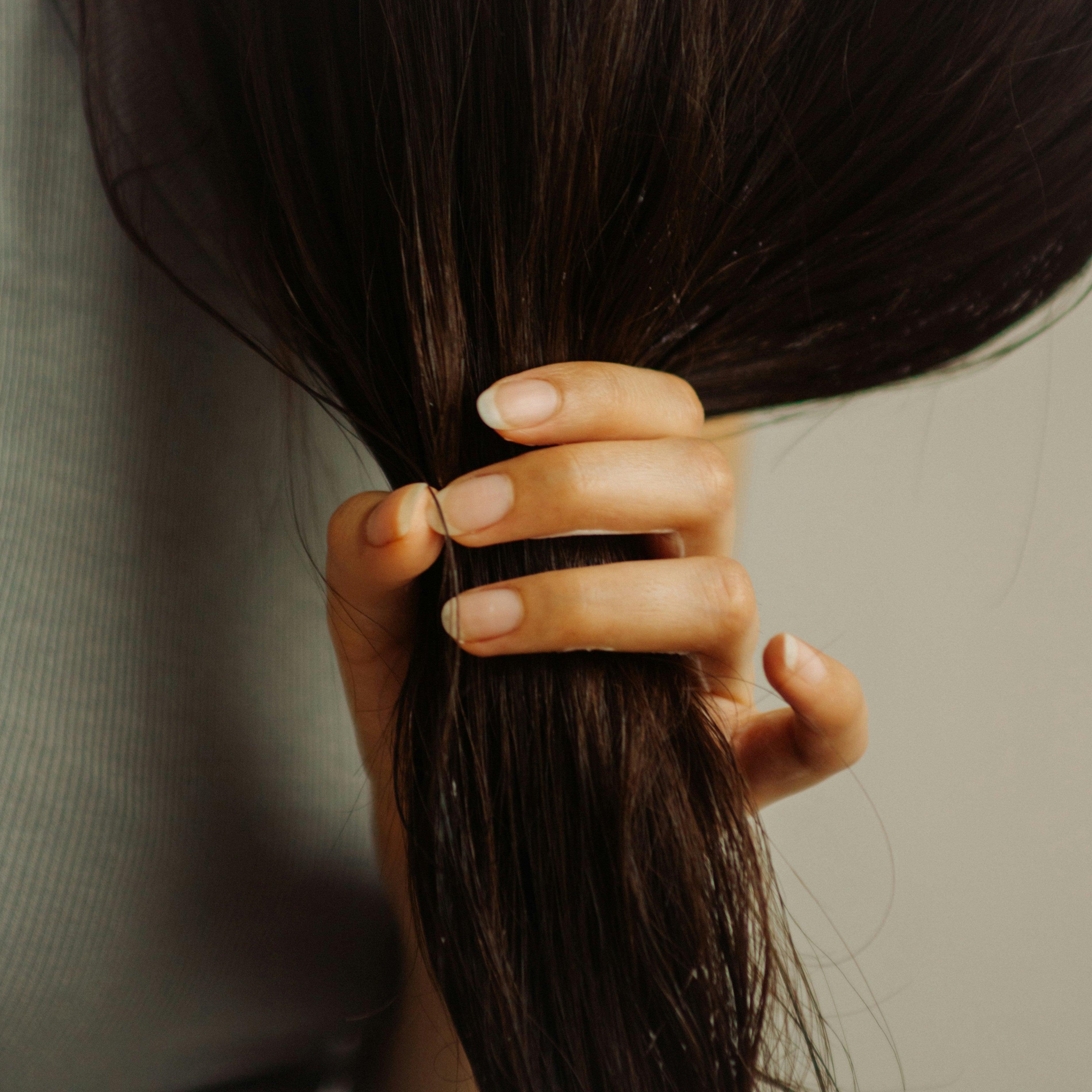 close-up of woman with healthy bare nails putting dark brown hair into a ponytail