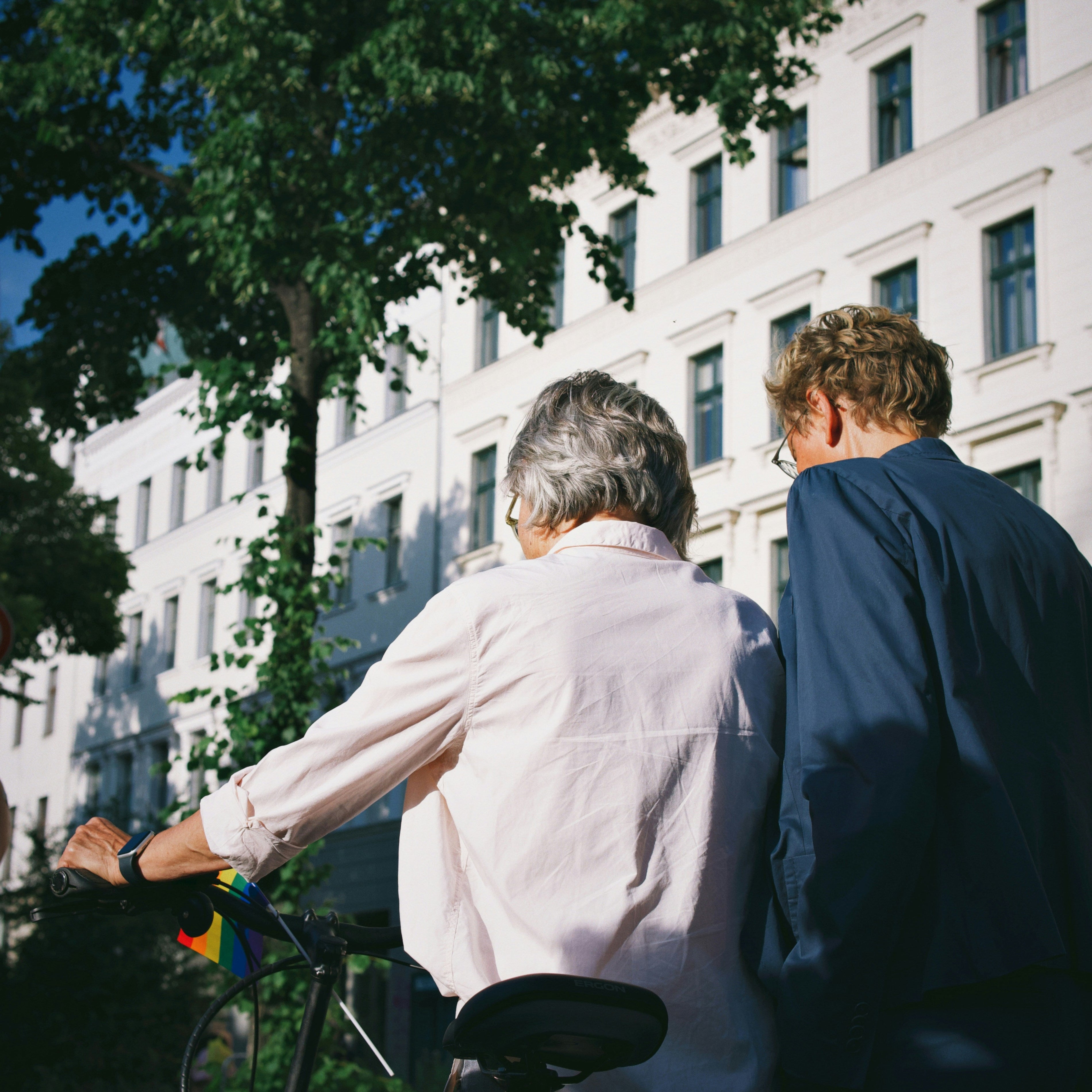 woman and man walking with bicycle in bright clean and verdant town square.